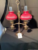 Full view of vintage two-arm lamp with red glass shades and brass body on black background.