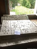 Stacked embossed tin tiles by a window showing fleur-de-lis pattern