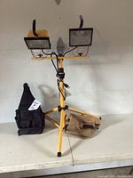 Adjustable dual head work light with yellow tripod stand, black and tan carrying bags on shelf