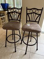 Front view of two metal barstools with brown upholstered seats and decorative backs.