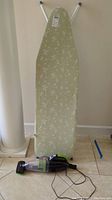 Photo of green floral ironing board standing upright with Bissell Pet Hair Eraser hand vacuum on the floor in front. Shows overall condition and scale of items.