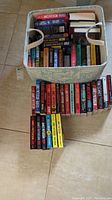 Top view of a fabric storage bin filled with multiple paperback and hardcover books, some books arranged in front of the storage bin.