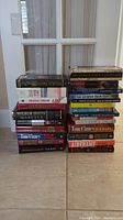 Two stacks of books including hardcovers and paperbacks from authors Tom Clancy, Wilbur Smith, Michael Crichton, Ken Follett, and others.