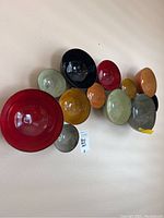 Side angled photo showing 11 metal bowls of varying sizes and colors attached together on backing to form wall art.