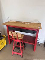 Full view of red Craftsman workbench with wooden top and matching red chair in front.
