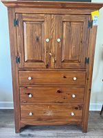 Front view of the wooden Ethan Allen armoire dresser showing two doors, three drawers with white knobs, and natural wood finish with some wear.