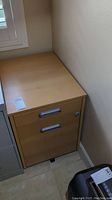 Angle view of the brown Ikea Galant filing cabinet showing two drawers with silver handles and a lock on the upper drawer.