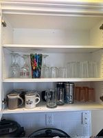 Wide shot of upper and lower shelves showing all glassware and mugs in the cabinet