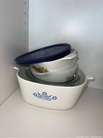 Stack of white ceramic and glass baking dishes with lid on top shelf