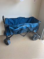 Front view of the blue collapsible cart with L.L. Bean logo, fabric and mesh pockets visible, sitting on concrete floor.