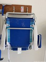 Folded Nautica beach chair showing white aluminum frame, attached storage pouch on side, and fabric seat.