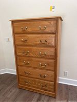 Front view of tall oak wood dresser with six drawers and brass handles, showing natural wood grain and condition.