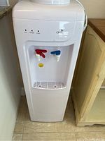 Full front view of the white Oasis water cooler showing the top water bottle area, front control panel with indicator lights, two spigots (red for hot, blue for cold), and drip tray.