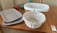 Four items on wooden table: two light gray rectangular serving platters, small round white basket, large rectangular wicker basket with fabric lining
