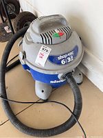 Front view of the Shop Vac unit showing logo, capacity, and motor horsepower on label, black hose connected on front.