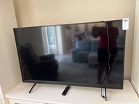Sony 57 inch flat screen TV showing front screen and stand legs, TV plugged in with power cord hanging.