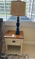 Overall view of the wooden side table with the blue antiqued lamp on top near a window.