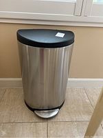 Full view of stainless steel trash can with black lid and foot pedal