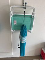 Folded turquoise fabric beach chair with white metal frame and carrying bag hanging from it