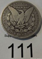 Reverse side of the 1899 O Morgan Silver Dollar showing eagle with wings outspread, surrounded by text and denomination.
