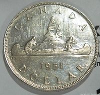 Reverse side of the 1951 Canada silver dollar coin featuring a canoe with two men and a mountainous background, along with date and currency inscriptions.