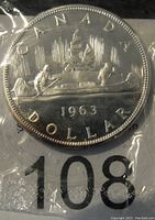 Obverse side of 1963 Canadian silver dollar showing the two canoeists with trees and sun rays, dated 1963 and the word CANADA DOLLAR.