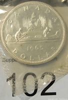 Reverse side of the 1965 Canadian silver dollar coin in sealed packaging showing the canoe design with two paddlers.