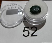 Oval dark green emerald gemstone approx 5.5 carats ready for jewelry use, resting in a round clear plastic case with white foam backing.