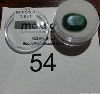 Top view of 7.5 carat emerald gemstone in a clear container showing natural inclusions and polished surface.