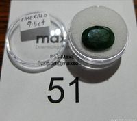 Top view of the 9.5 carat oval emerald gemstone in a clear display case with label visible