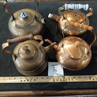 Top view of all four copper teapots arranged closely on a black surface with a measuring stick showing sizes up to 12 inches.