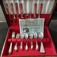 Full silverware set in red velvet case showing knives, forks, spoons, and paper certificate.