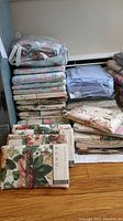 Stacks of new packaged floral and solid blue bedding on hardwood floor