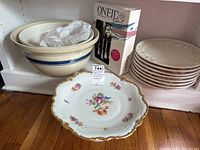Photo showing three cream bowls with blue stripes, boxed Oneida flatware and eight stacked pink Pier 1 plates