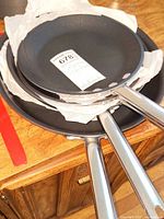 Stack of four Calphalon commercial cookware frying pans with stainless steel handles, showing the two shallow and two deeper pans separated by white paper.