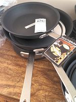 Stack of three Calphalon frying pans showing the shiny metal handles and black non-stick interior surface with Calphalon tag visible.
