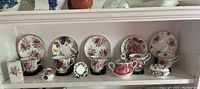 Photo showing a collection of fine bone china teacups and matching saucers with floral patterns, plus a pink sugar bowl, creamer or small teapot, egg-shaped trinket box.