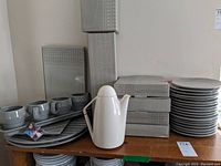Overall view of grey ceramic cups on oblong tray, teapot, stacked plates and packaging boxes