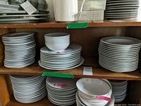 Shelves with stacks of white ceramic dinnerware including bowls, saucers, and plates.