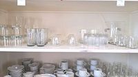Shelf of assorted water glasses, stemware, clear cups and white cups with saucers
