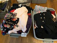 Two plastic totes filled with assorted ladies sweaters, tops, and dresses in various colors and patterns.