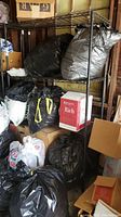 Front view of black metal shelving unit loaded with various items including black garbage bags and boxes.