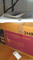 Original product box showing Sharp microwave oven description: .9 Cu. Ft., 800W, Smart & Easy sensor features, automatic popcorn key, minute plus, instant start operation.