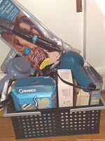 Personal care electrical appliances piled in a black plastic basket including two hair dryers (teal and grey), Norelco shaver box, cords and other appliances