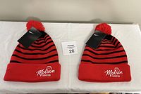 Two red and black striped Nike winter tuques with Molson Canadian embroidery and red pom-poms, laid side by side showing front cuff design and Nike tags.