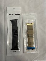 Photo of two Apple Watch bands in their packaging, one black sport band and one gold metal mesh band.