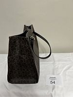 Side view of the Calvin Klein purse showing the brown monogram fabric and one black handle.