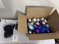 Photo showing coiled indoor string lights with attached control switch alongside an open box containing mixed Christmas bulbs.