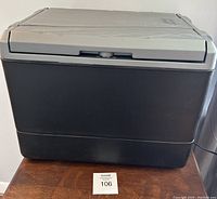 Front and side view of Coleman plug-in cooler showing dark gray body and light gray lid with latch and embossed design details.