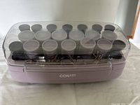 Top view of 20 electric curlers arranged in purple heating base with clear lid showing curled rollers and clips inside